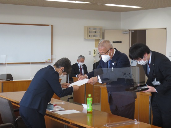 席をパーテンションで区切られた会議室で、委嘱書を手渡ししている三郷市長と交付のサポートをしている男性、委嘱書を受け取っている委員の女性の写真