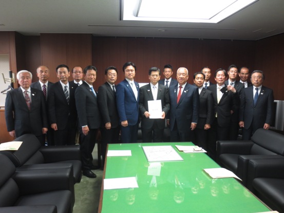 要望書を手に持った石井啓一氏と三郷市、三郷市議会、埼玉県、埼玉県議会、三郷市商工会、JAさいかつの代表者が壁の前に並んで立ち記念撮影をしている写真