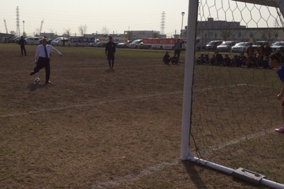 上着を脱いだ市長がサッカーゴールに向かってボールを蹴ろうとしている始球式の様子の写真