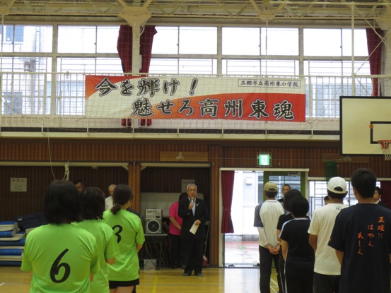 「今を輝け!魅せろ高州東魂」と書かれた横断幕が設置されている体育館で、関係者たちが整列し市長が挨拶をしている写真