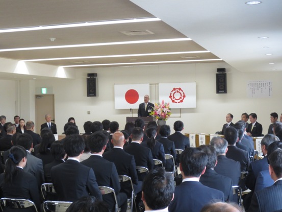 ずらりと並んだパイプ椅子にスーツ姿の教職員が座っている部屋で、正面の演台に立って話をしている市長の写真