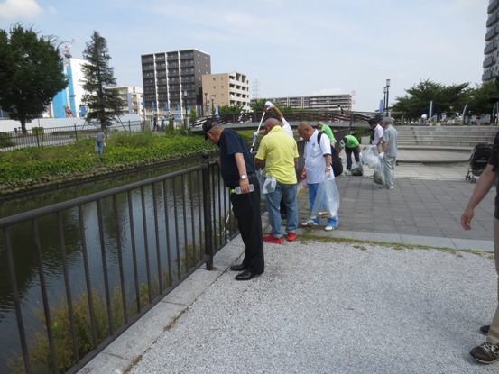 川沿いに設置されたフェンス横の道路でたくさんの参加者たちとともに川の方を見つめいている市長の写真