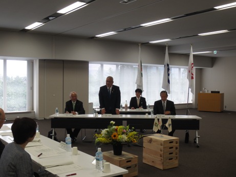 長机が設置された室内で、中央に座っていた席から立ち上がり挨拶を行っている市長の写真