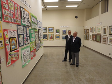 文化会館の会場の壁いっぱいに展示されている絵画などの作品を男性と市長が鑑賞している様子の写真