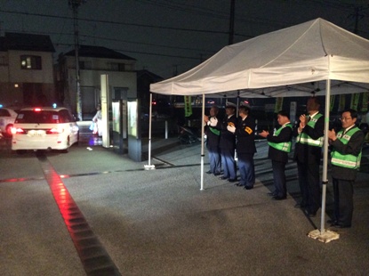 敷地内の入り口右側に設置した白色のテントの中に6名の関係者が横一列に並び拍手をしながら青パトを見送っている様子の写真