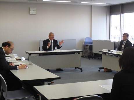 白い長机が口の字型に置かれており、それぞれの机に出席者が着席する中、出席者の方へ向かって話をしている市長を正面から写した写真