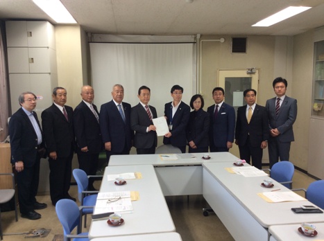 テーブルが並んでいる室内奥で市長を含め10名の関係者が横一列に並び中央の浅井県土整備部長と右側の男性が一緒に要望書を持っている写真