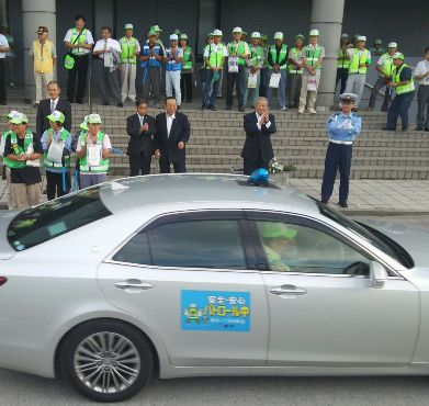 「安全・安心パトロール中」と書かれたシールが貼られた車に向かって市長や警察署長、参加者が拍手を送っている「青色防犯パトロール出発式」の様子の写真