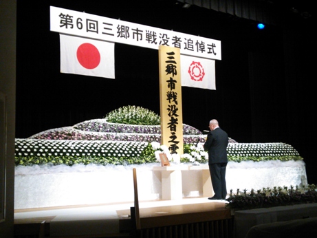 「第6回三郷市戦没者追悼式」と書かれた横断幕の下で哀悼の誠を捧げている市長の後ろ姿の写真