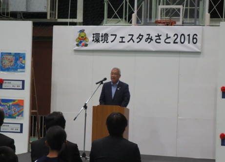 「環境フェスタみさと2016」と書かれた横幕が貼られた会場の演壇で挨拶を行っている市長の写真
