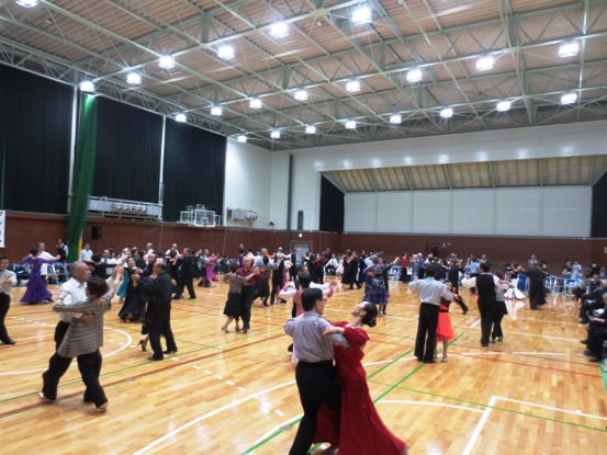 体育館で衣装を着た多くの参加者たちが社交ダンスを踊っている写真