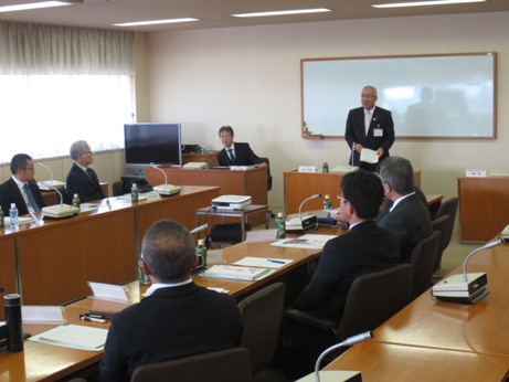 会議室のホワイトボードが設置された壁を背に、議会会長席の後ろに立った市長が、手前側に2列並んだ机に向かい合って座っている委員の方を向いて話をしている写真