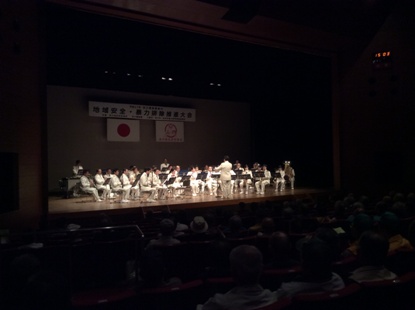 ステージで白色の衣装を着た埼玉県警察音楽隊の皆さんが演奏を行っている様子の写真
