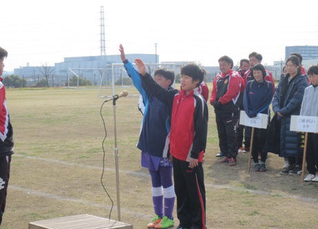 お立ち台のそばに立ち右手を上げ男性に向かって選手宣誓する2名の男の子と、後ろに立って見守るプラカードを持った選手たちの写真
