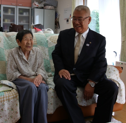 自宅のソファに笑顔の塚越さんと市長が並んで座っている写真