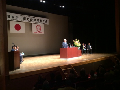 「吉川警察署管内地域安全暴力排除推進大会」と書かれた横断幕が飾られたステージの檀上で挨拶を行っている市長の写真