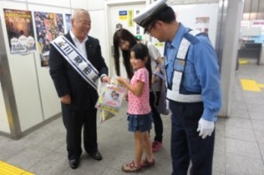 市長と吉川警察署長に挟まれた母親と女の子が交通安全啓発グッズの袋を手渡され笑顔で立っている写真