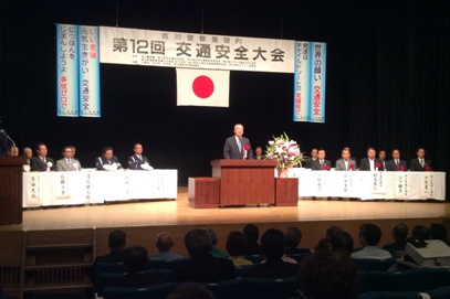「第12回交通安全大会」と書かれた横断幕の下ステージの演壇で挨拶を行っている市長の写真