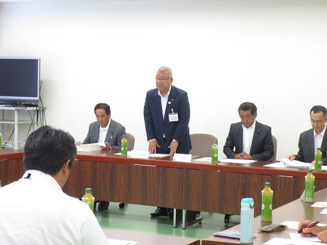 平成29年度第1回四市町農政研究会にて、立って挨拶の言葉を述べる三郷市長とロの字型に配置されペットボトルのお茶が置かれた席に座り話を聞く参加者の写真