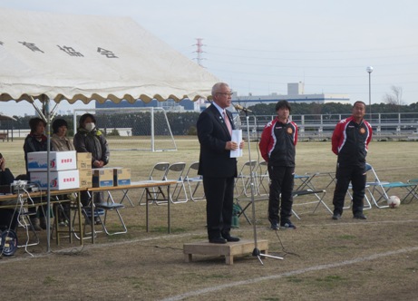 白いテントの前に設置されたお立ち台の上に立ち挨拶の言葉を述べる三郷市長と、テント付近に立ち話を聞く関係者の写真