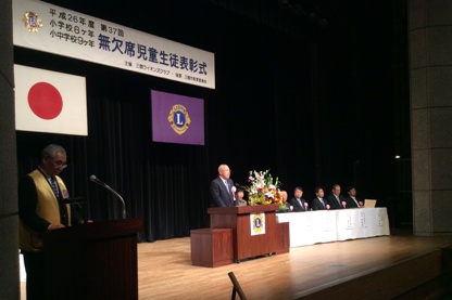 「無欠席児童生徒表彰式」と書かれた横断幕の下に国旗と三郷市市旗が飾られたステージの檀上でお祝いの言葉を話している市長の写真