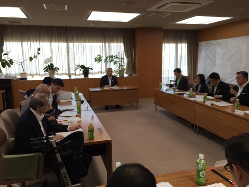 窓側の席に座っている市長が話を行っているのを会議の参加者が聞いている様子の写真