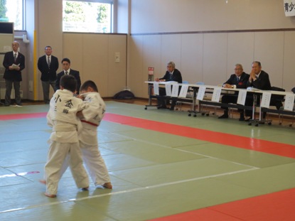 柔道場で組み合って競技を行っている2名の子どもの試合の様子の写真