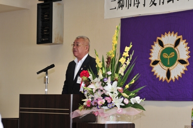 演壇に設置されたマイクの前で挨拶を行っている市長を右斜めから撮影した写真