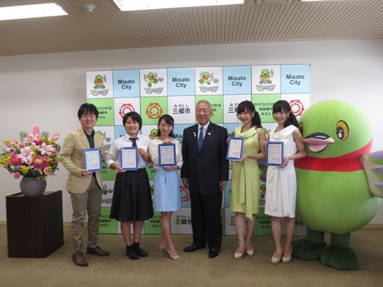 三郷市のバックボードの前で、市長を中心に5名の三郷市PR大使のかたと、かいちゃんが横一列になって記念撮影をしている写真