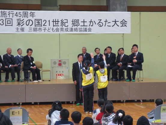 来賓や大会関係者が着席している舞台を背にして立っているスーツ姿の男性に向かって、黄色いゼッケンを着た2名の選手代表が右手を上げて選手宣誓をしている写真