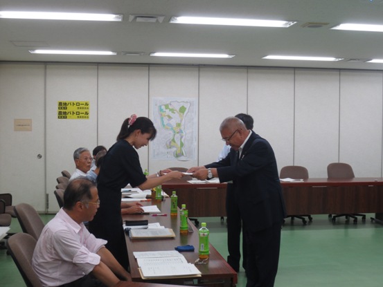会議室に設置された2台の長机に5名の方が座り、席から立ち上がった手前から2番目の女性が市長から委託書を交付されている様子の写真
