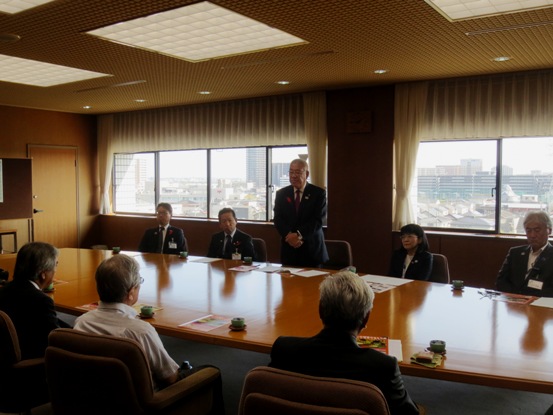 横長の大きなテーブルの手前に三郷中央ロータリークラブの方々が座り、向かい合った席の市長が立ち上がり挨拶を行っている様子の写真