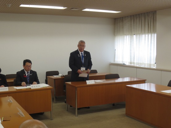 3名掛けの長机の席から立ち上がり挨拶を行っている市長の写真