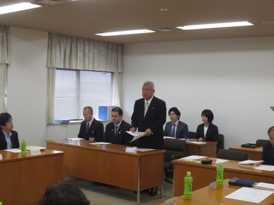 3名掛けの机が2列に並び手前の右端の席から立ち上がり挨拶を行っている市長の写真