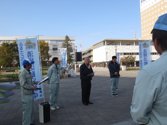 公園の広場に設置されたのぼり旗の間に立っている市長が挨拶を行っている様子の写真