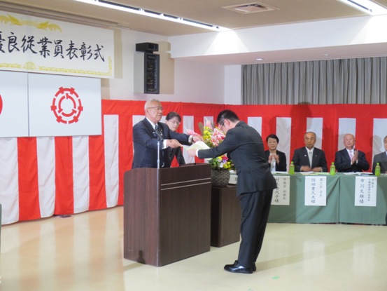 右奥に関係者が座り拍手を送るなか、演壇を挟んで男性に市長が賞状を渡している表彰の様子の写真