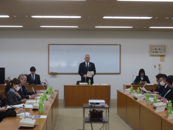 ホワイトボードの前に3つの机が並べられ、中央の席から立ち上がり挨拶をしている市長の話を聞いている協議会の参加者の人達を写した写真