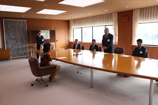 吉田選手と横長のテーブルを挟んで職員が座り、立ち上がった市長が挨拶を行っている様子の部屋を写した写真