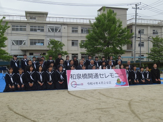 北中学校の生徒と三郷市長や関係者の方々が横3列に並び、前列中央の方が「和泉橋開通セレモニー」と書かれたプレートを持ち一緒に記念撮影をしている写真