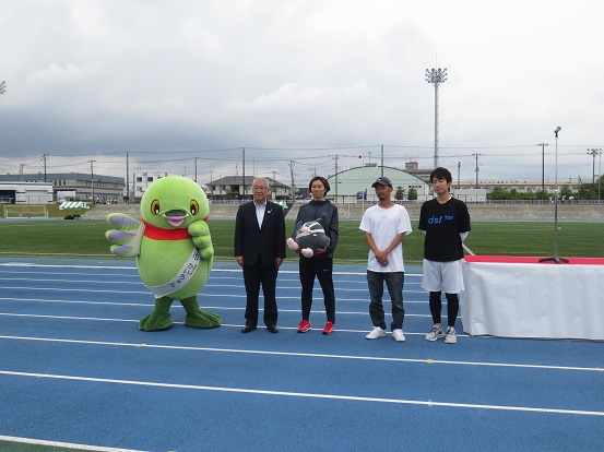 三郷市陸上競技場でかいちゃん、三郷市長、3人の講師の方々、つぶちゃんが一緒に記念撮影をしている写真