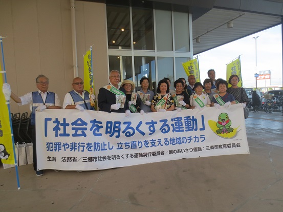 街頭啓発活動に参加された方々と三郷市長が一緒に「社会を明るくする運動市内街頭啓発活動」と書かれた横断幕を持って記念撮影をしている写真