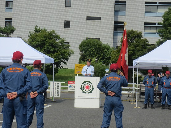 屋外の消防隊員が整列している正面で、設置された演壇に立って、制帽を被った市長が話をしている写真