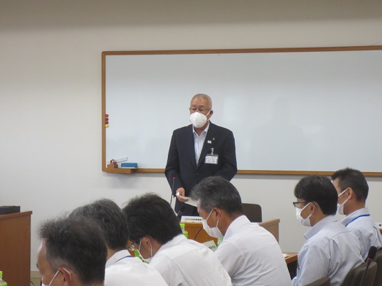 長机に関係者たちが着席しているなか、市長が正面に立って資料を手に話をしている写真
