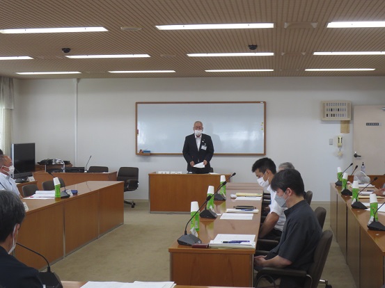 長机が向かい合わせに並んでいる部屋に関係者が着席しているなか、部屋の正面に立って資料を手に話をしている様子の市長の写真