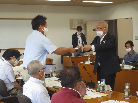 長机が並べられている部屋に多くの関係者が着席しているなか、1名の男性が市長から委嘱書を交付されている写真