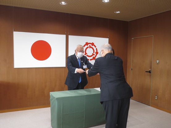 日本国旗と三郷市旗が下げられている部屋で、市長が関係者へ任命書を交付している写真