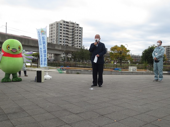 屋外の広場で、かいちゃんや関係者が見守る中、市長がマイクを手に話をしている写真