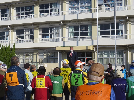 高州小学校の校舎を背景に、グラウンドでゼッケンを着けた参加者たちの前に立って話をしている市長の写真