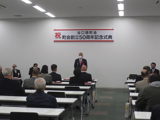 谷口南町会創立50周年記念式典の吊り看板が設置された部屋で、市長が出席者たちの前に立って話をしている写真