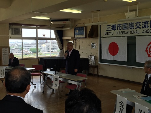 長机の中央に「議長」と書かれた紙が貼られた席から立ち上がり、右手にマイクを持ち挨拶を行っている市長の写真